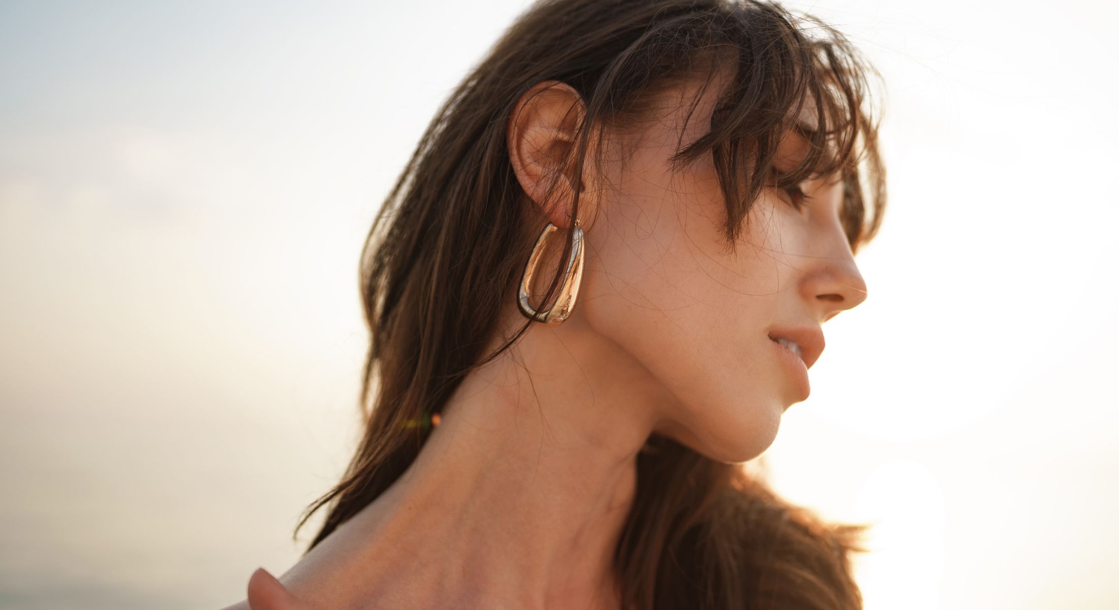 Laguna Niguel Hydrafacial model wearing elegant earrings against a sunset backdrop.
