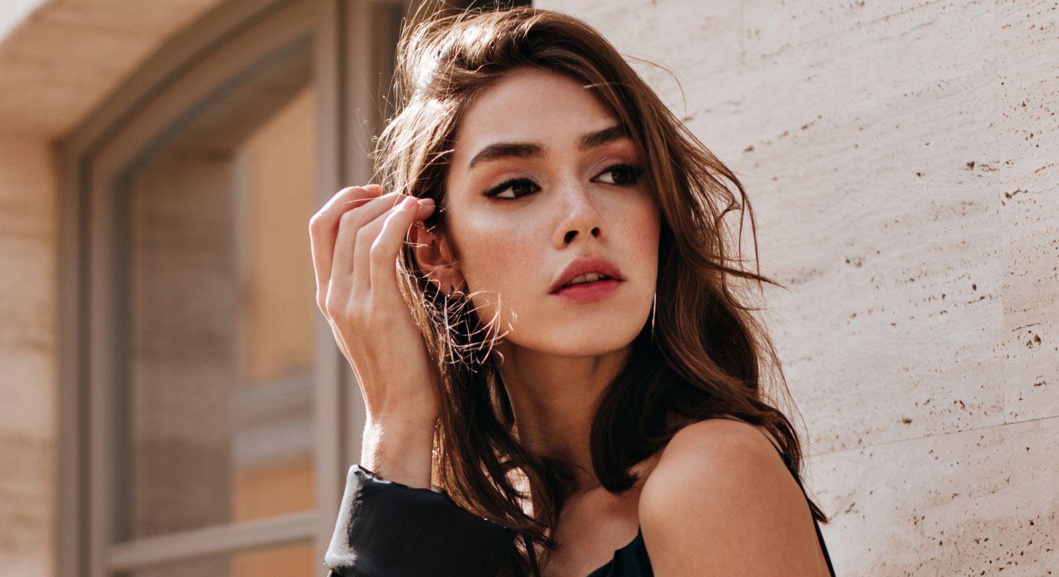 Orange County lip blushing model with tousled hair against textured wall.